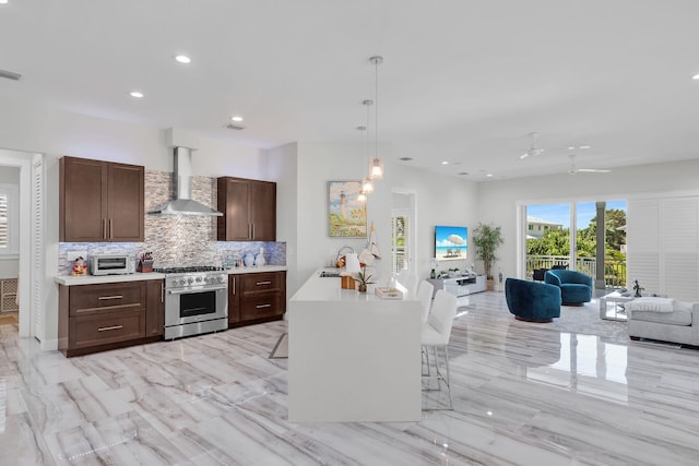 kitchen featuring stainless steel range, light countertops, open floor plan, a sink, and wall chimney range hood