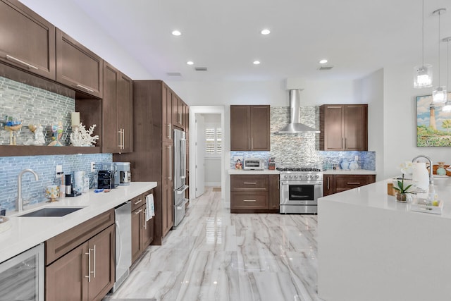 kitchen with a sink, light countertops, appliances with stainless steel finishes, and wall chimney range hood