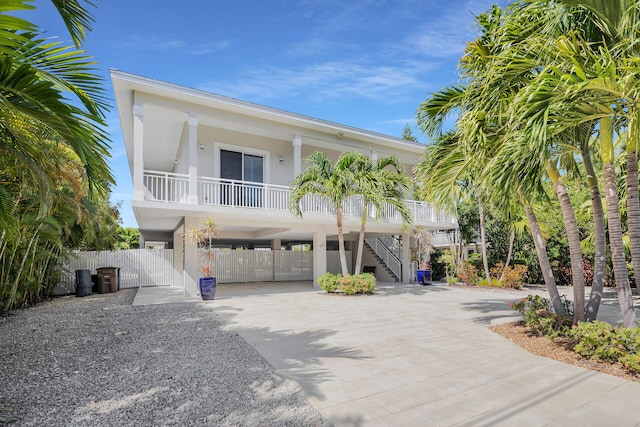 raised beach house featuring stairs, driveway, a gate, stucco siding, and a carport