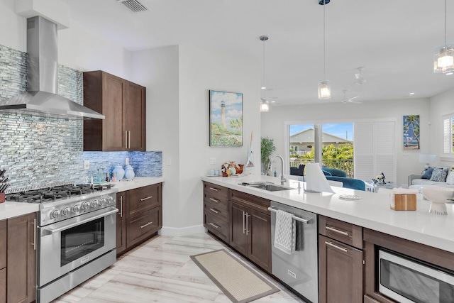 kitchen featuring tasteful backsplash, wall chimney exhaust hood, appliances with stainless steel finishes, light countertops, and a sink