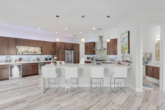 kitchen with a breakfast bar area, beverage cooler, high end refrigerator, light countertops, and wall chimney range hood