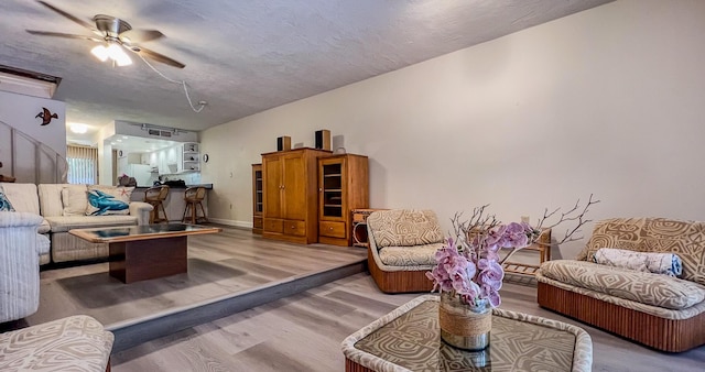 living room featuring a textured ceiling, wood-type flooring, and ceiling fan