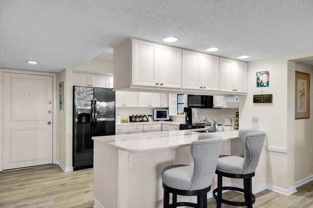 kitchen with black appliances, light wood-type flooring, a kitchen breakfast bar, kitchen peninsula, and white cabinets