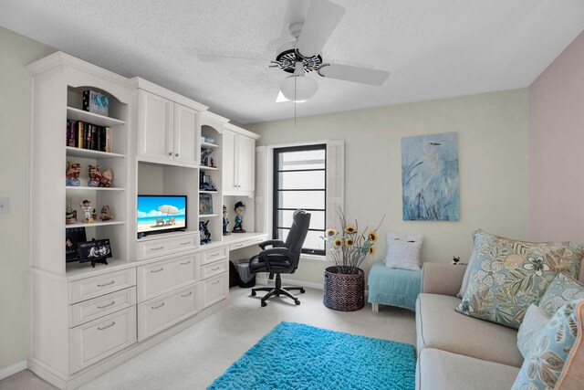 carpeted office space with ceiling fan, built in desk, and a textured ceiling
