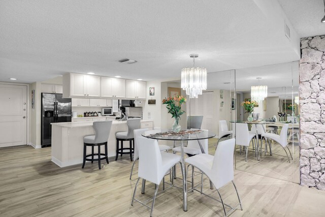 dining space featuring a notable chandelier, a textured ceiling, and light hardwood / wood-style flooring
