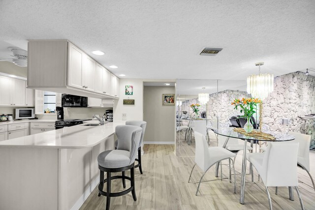 kitchen with hanging light fixtures, sink, kitchen peninsula, and white cabinets