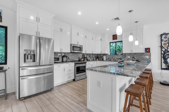 kitchen with pendant lighting, a kitchen breakfast bar, stainless steel appliances, white cabinets, and dark stone counters