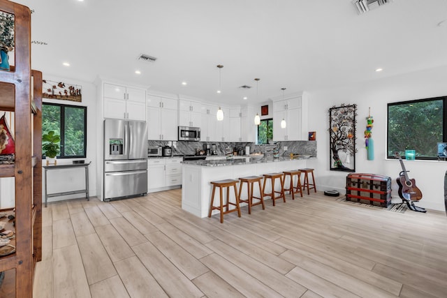 kitchen with light stone counters, tasteful backsplash, kitchen peninsula, stainless steel appliances, and white cabinets