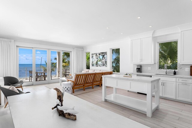 kitchen featuring sink, a water view, tasteful backsplash, light wood-type flooring, and white cabinets