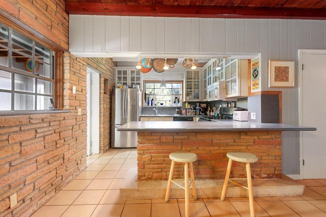 bar featuring light tile patterned flooring, brick wall, beamed ceiling, white cabinetry, and stainless steel fridge