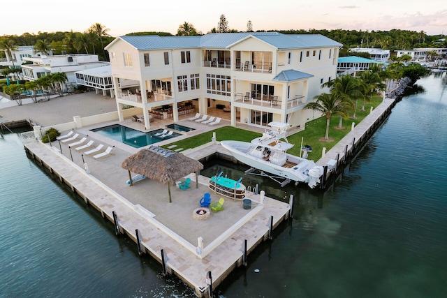 back house at dusk with a gazebo, a patio, a water view, a pool with hot tub, and a balcony