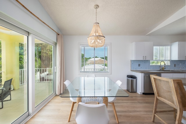 dining space with a notable chandelier, vaulted ceiling, a textured ceiling, and light wood-type flooring