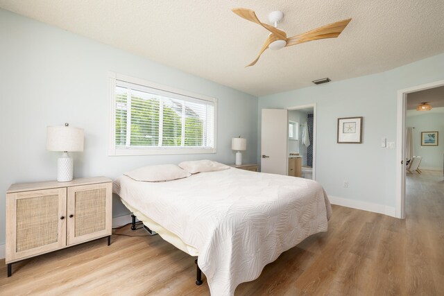 bedroom with ceiling fan, ensuite bath, a textured ceiling, and light wood-type flooring