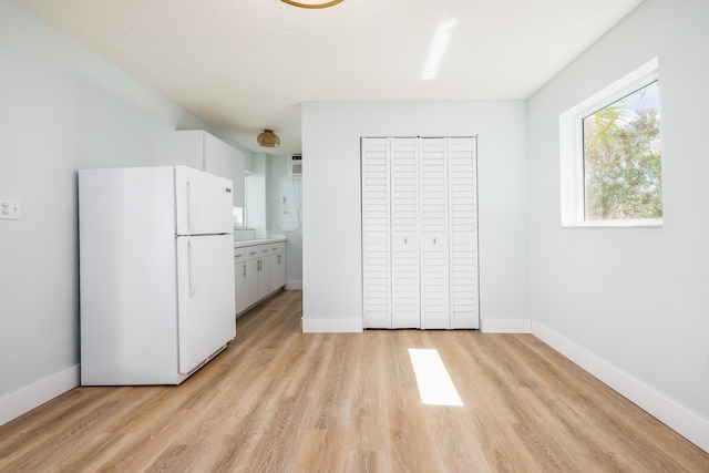unfurnished bedroom featuring a closet, a textured ceiling, white fridge, and light hardwood / wood-style flooring
