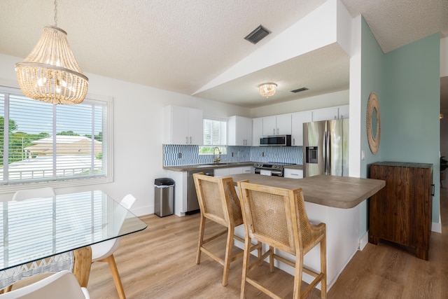 kitchen featuring appliances with stainless steel finishes, white cabinetry, hanging light fixtures, backsplash, and vaulted ceiling