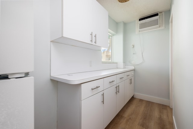 kitchen with an AC wall unit, hardwood / wood-style floors, white cabinets, and a textured ceiling