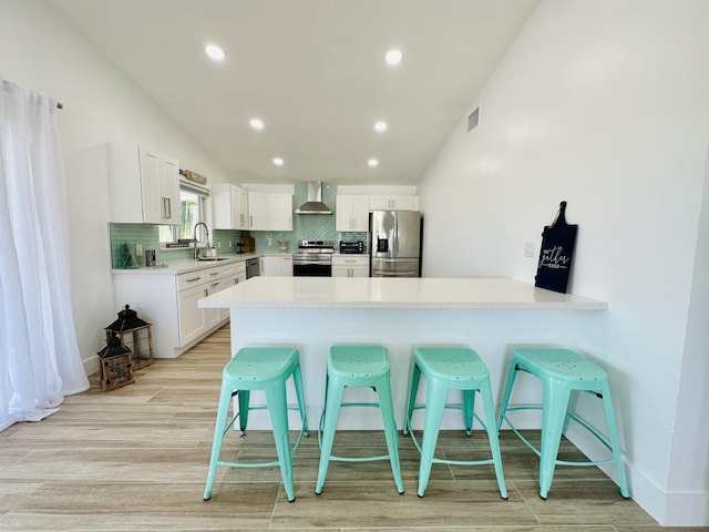 kitchen featuring sink, a breakfast bar area, white cabinets, stainless steel appliances, and wall chimney range hood