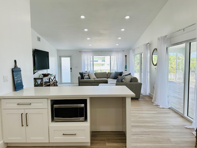 kitchen featuring vaulted ceiling, kitchen peninsula, light hardwood / wood-style floors, and white cabinets