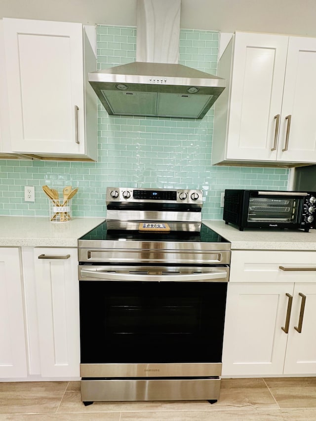 kitchen with white cabinetry, wall chimney range hood, stainless steel range with electric cooktop, and decorative backsplash