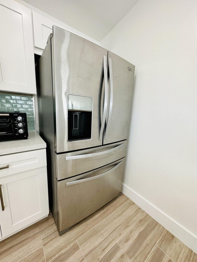 kitchen with white cabinetry, stainless steel refrigerator with ice dispenser, light hardwood / wood-style flooring, and decorative backsplash