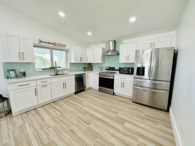 kitchen with vaulted ceiling, sink, white cabinets, stainless steel appliances, and wall chimney exhaust hood