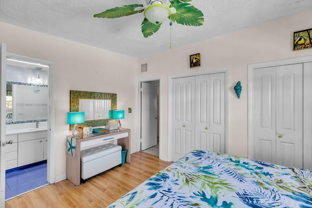 bedroom featuring a sink, ensuite bath, light wood-style floors, two closets, and visible vents