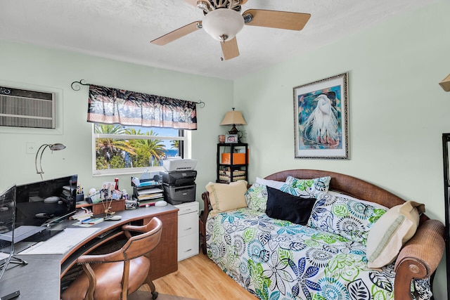 bedroom with light wood-style flooring, ceiling fan, and a wall mounted AC