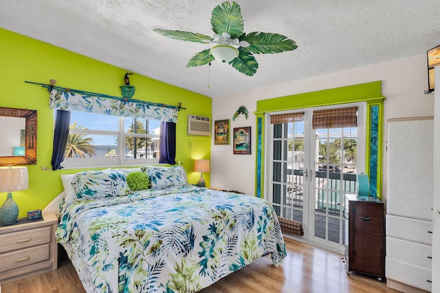 bedroom with access to outside, a textured ceiling, a wall unit AC, and wood finished floors