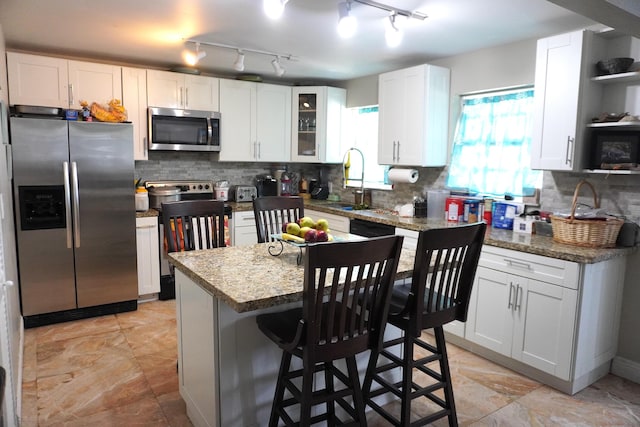 kitchen with stone counters, a kitchen island, white cabinets, and appliances with stainless steel finishes