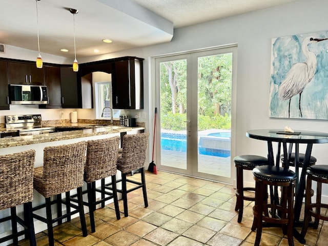 kitchen featuring stainless steel appliances, dark brown cabinetry, light stone countertops, decorative light fixtures, and a kitchen bar