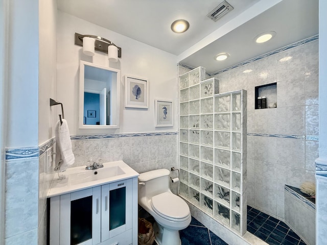 bathroom featuring tile patterned flooring, a tile shower, tile walls, toilet, and vanity