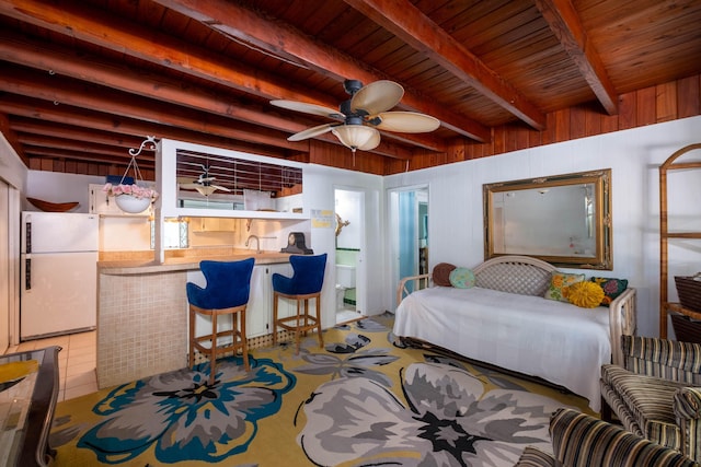 bedroom featuring freestanding refrigerator, beam ceiling, wooden ceiling, wood walls, and a sink