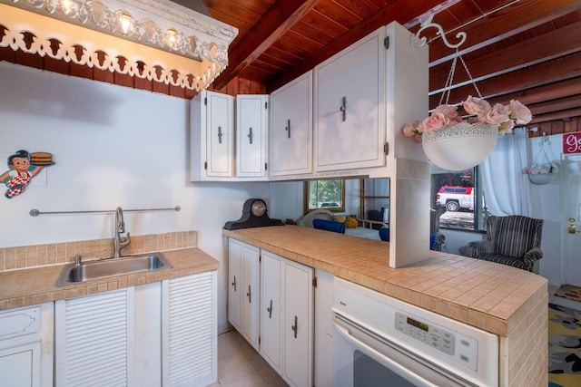 kitchen with a sink, wooden ceiling, white cabinets, beamed ceiling, and oven