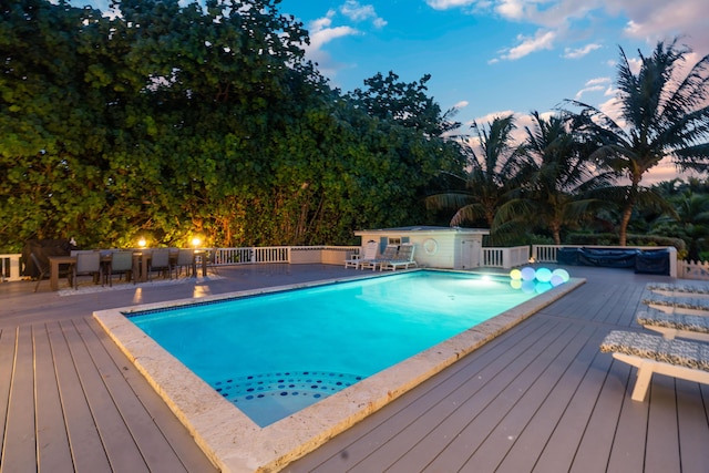 pool at dusk featuring a deck and an outdoor bar