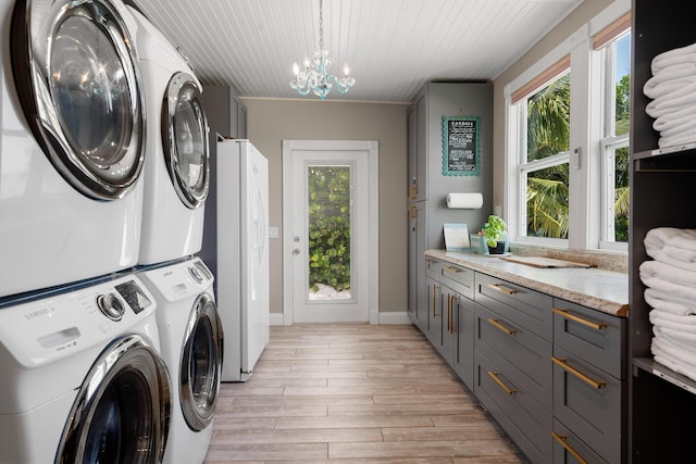 washroom featuring a notable chandelier, light hardwood / wood-style floors, and stacked washer and clothes dryer