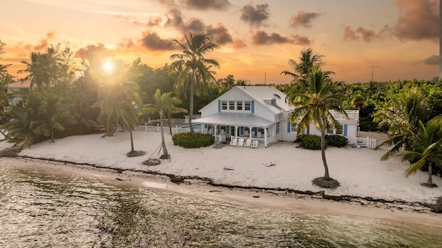 back house at dusk featuring a water view and a beach view