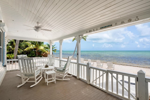 wooden deck featuring a view of the beach, a water view, and ceiling fan