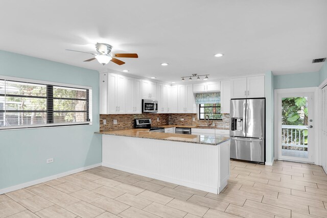 kitchen featuring appliances with stainless steel finishes, light stone counters, tasteful backsplash, white cabinets, and kitchen peninsula