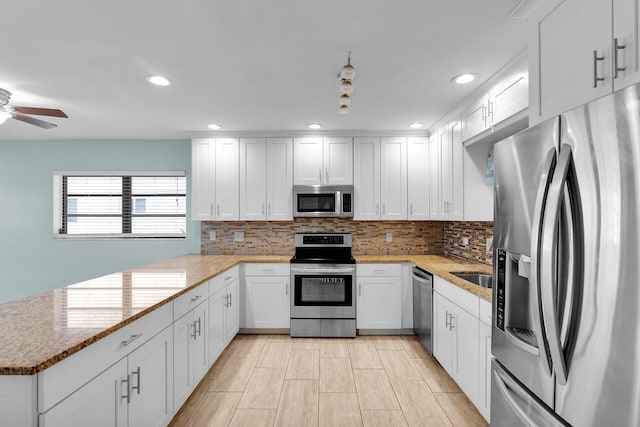 kitchen with tasteful backsplash, kitchen peninsula, stainless steel appliances, light stone countertops, and white cabinets