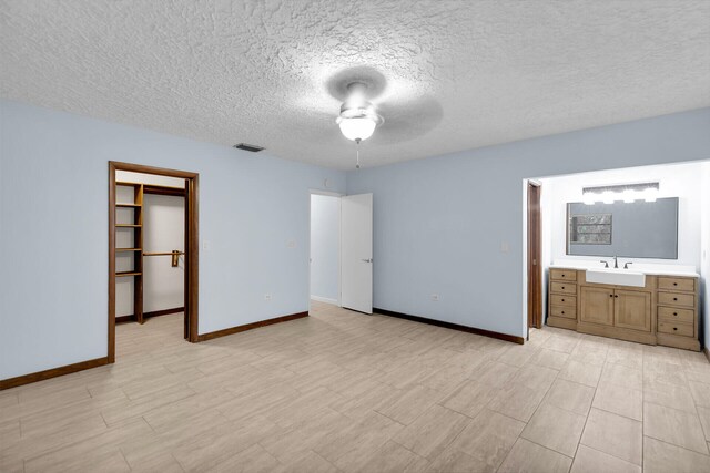 unfurnished bedroom with a walk in closet, sink, a textured ceiling, and light wood-type flooring