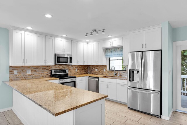 kitchen featuring sink, appliances with stainless steel finishes, white cabinetry, light stone counters, and kitchen peninsula