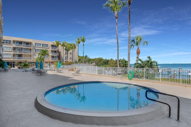 pool featuring a patio, a water view, and fence