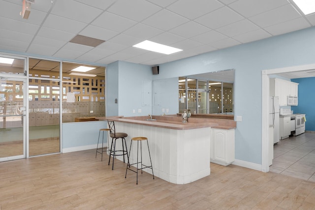 kitchen featuring a breakfast bar area, a paneled ceiling, white cabinets, light wood-type flooring, and white appliances