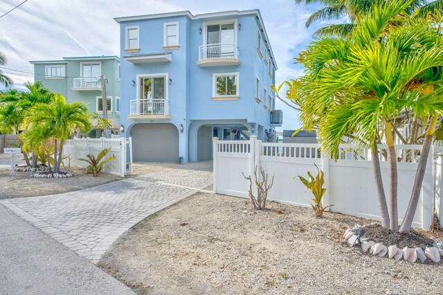 coastal home featuring a fenced front yard, stucco siding, decorative driveway, and a balcony