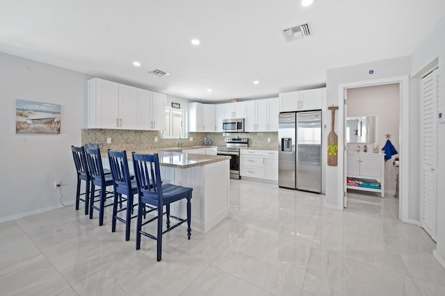 94825 Overseas Hwy Unit 185, Key Largo, FL 33037 - kitchen with appliances with stainless steel finishes, a peninsula, a kitchen breakfast bar, tasteful backsplash, and white cabinetry