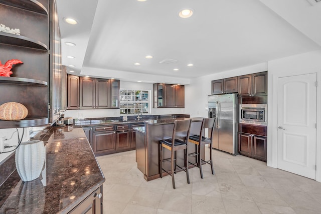 kitchen with a breakfast bar area, appliances with stainless steel finishes, dark brown cabinets, a center island, and dark stone counters