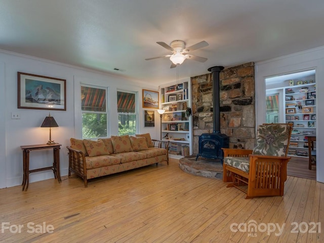 living room featuring light hardwood / wood-style flooring, a wood stove, ceiling fan, and built in shelves