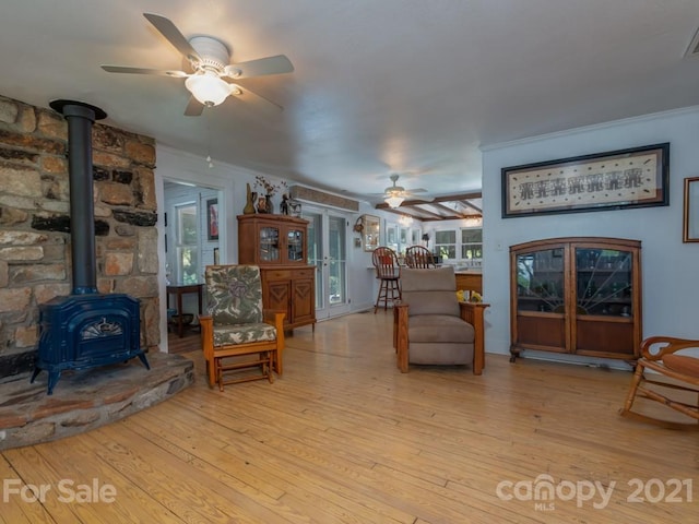 living room featuring crown molding, ceiling fan, a wood stove, and light wood-type flooring