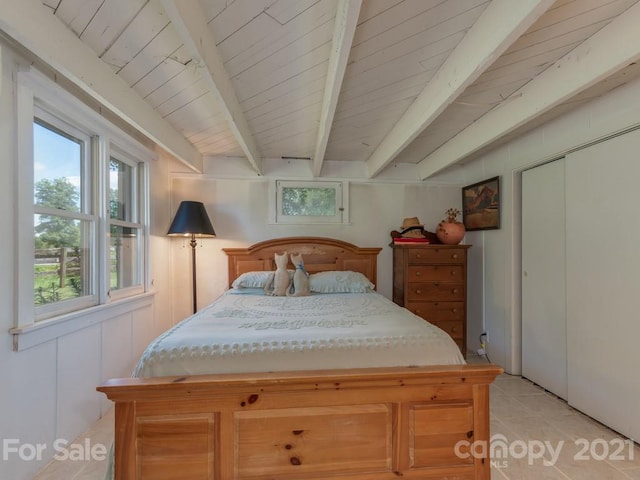 bedroom featuring light tile floors, beamed ceiling, and a closet