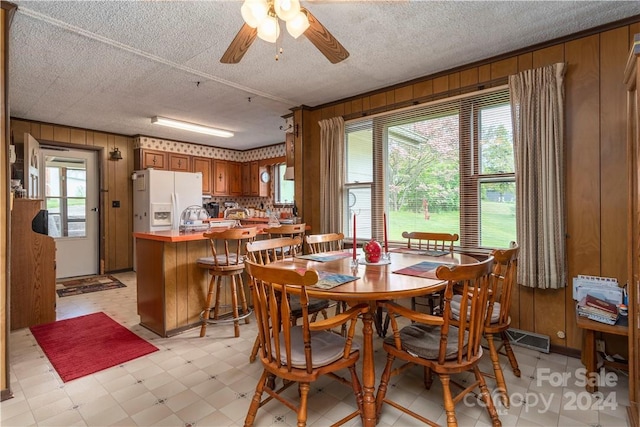 dining room with ceiling fan, plenty of natural light, and wooden walls